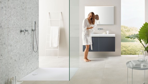 Donna che si asciuga i capelli con un asciugamano in un bagno con doccia aperta e grandi piastrelle in stile terrazzo Donna che si asciuga i capelli con un asciugamano in un bagno con doccia aperta e grandi piastrelle in stile terrazzo