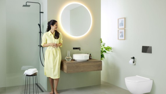 Donna in abito giallo in piedi davanti a un bagno verde menta con mobili e sanitari di Geberit e rubinetti neri
