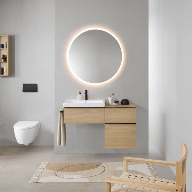 Bagno con pareti grigie, mobili da bagno Geberit in legno e specchio rotondo Geberit Option illuminato