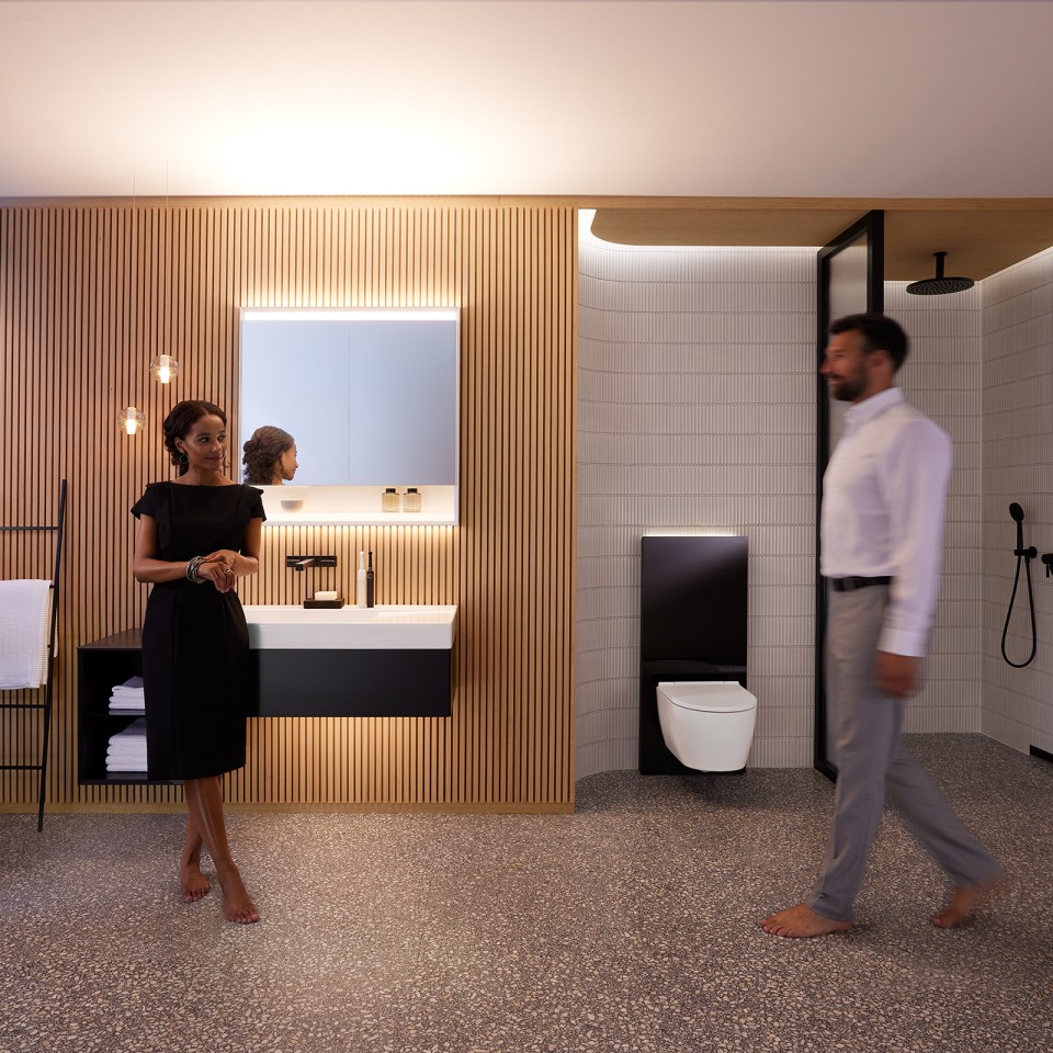 Un homme et une femme dans une salle de bains harmonieusement éclairée avec les meubles de salle de bains et les céramiques Geberit ONE (© Geberit)