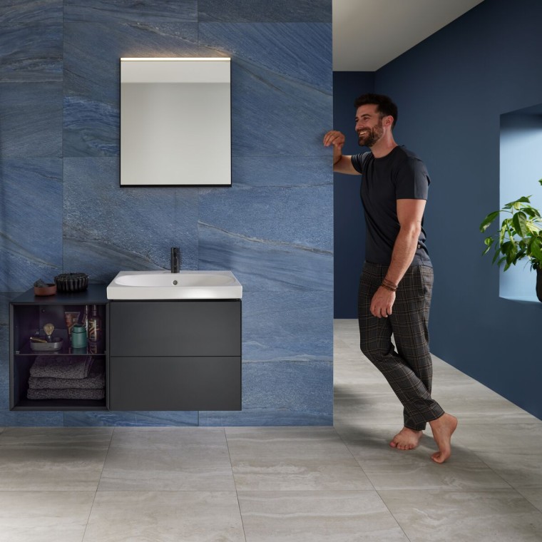 Uomo appoggiato alla parete in un bagno blu con lavabo Geberit Mix & Match Uomo appoggiato alla parete in un bagno blu con lavabo Geberit Mix & Match