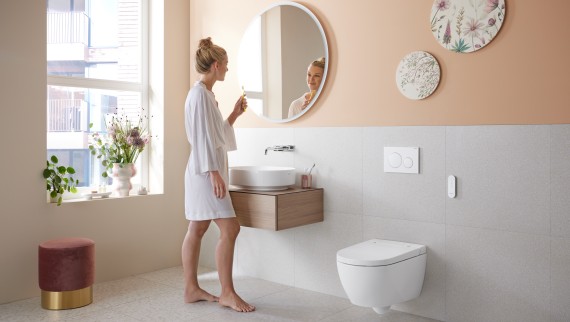 Frau in Badezimmer mit Geberit AquaClean Alba, einer kostengünstigen Toilette mit Waschfunktion Frau in Badezimmer mit Geberit AquaClean Alba, einer kostengünstigen Toilette mit Waschfunktion