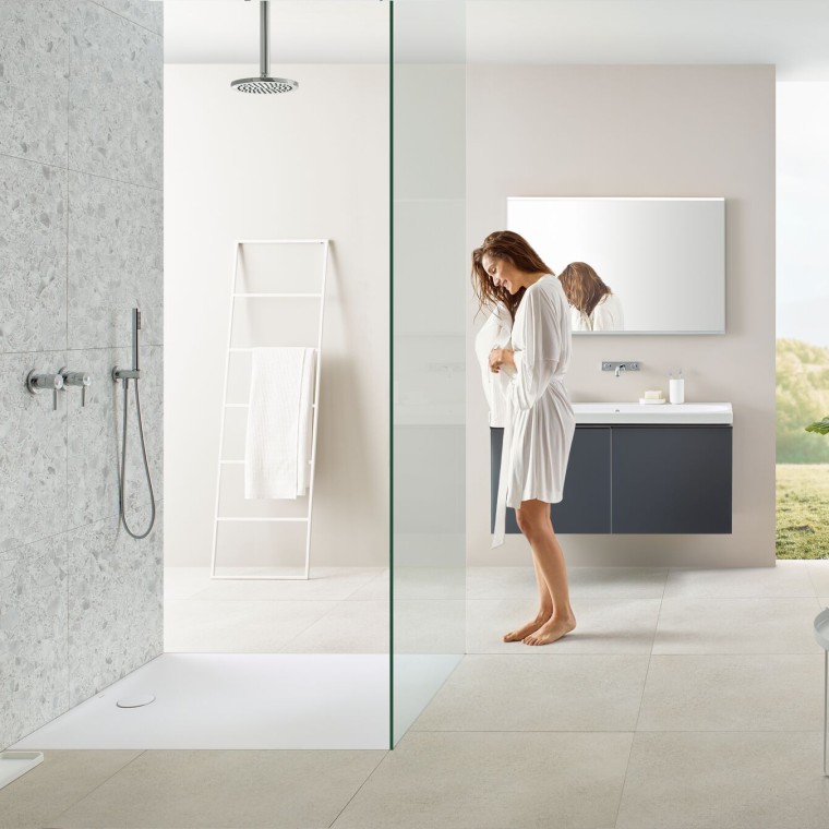 Femme dans une salle de bains avec douche de plain-pied et receveur de douche Geberit Olona Femme dans une salle de bains avec douche de plain-pied et receveur de douche Geberit Olona