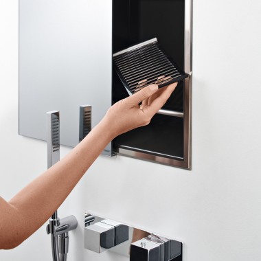 Une main féminine insère une tablette dans une niche de rangement dans la douche (© Geberit)