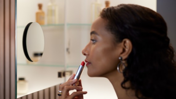 Une femme applique du rouge à lèvres devant un miroir grossissant (© Geberit)