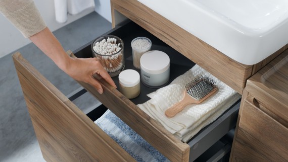 Une main ouvre l’un des tiroirs du meuble sous lavabo Geberit Renova Plan, design bois naturel
