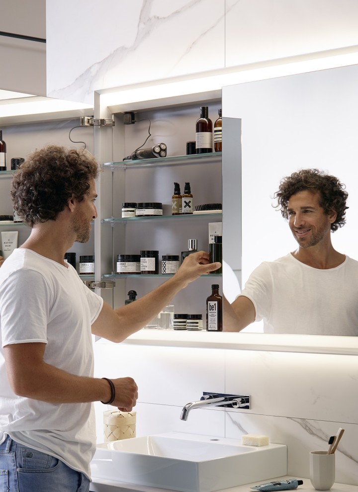 Un homme se tient dans une salle de bains équipée d’une armoire de toilette Geberit ONE