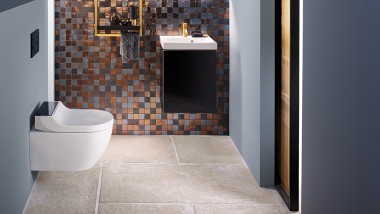 Vista su un moderno WC degli ospiti con un AquaClean Tuma Comfort e un lavabo Acanto davanti a una parete posteriore in mosaico.