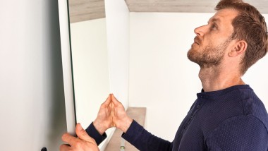 Un homme accroche un miroir Geberit Option au cours de la rénovation d’une salle de bains
