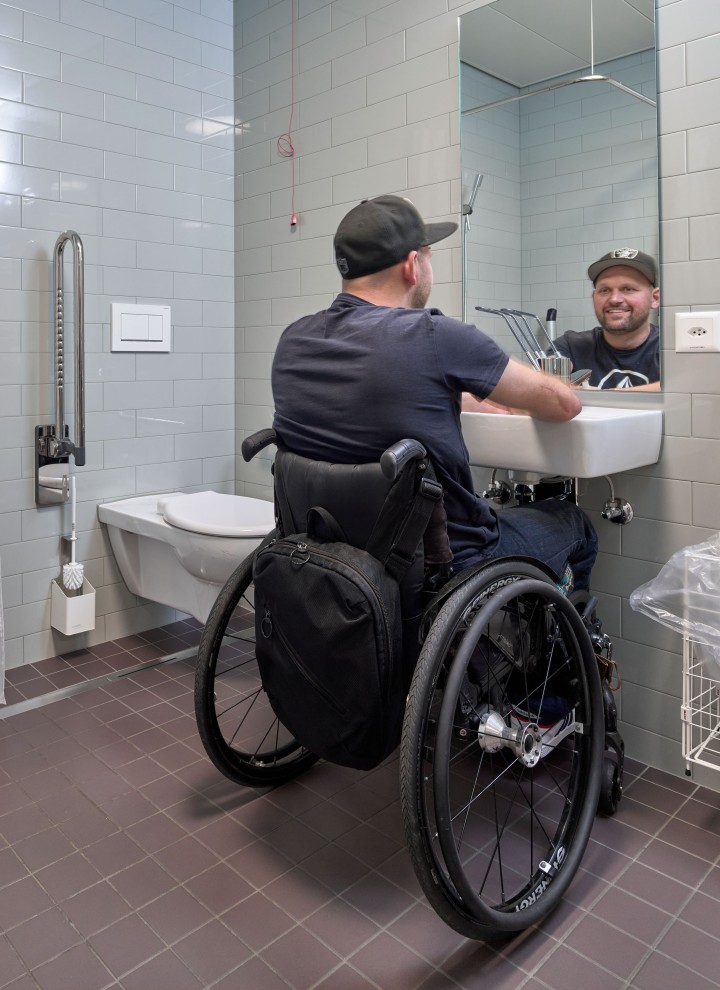 Peter Roos en fauteuil roulant au lavabo dʼune salle de bains adaptée aux personnes à mobilité réduite (© Ben Huggler)