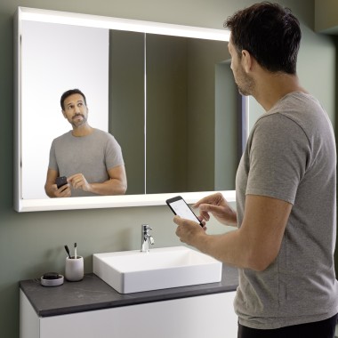 Un homme commande l’éclairage de l’armoire de toilette Geberit ONE à l’aide de son smartphone (© Geberit)