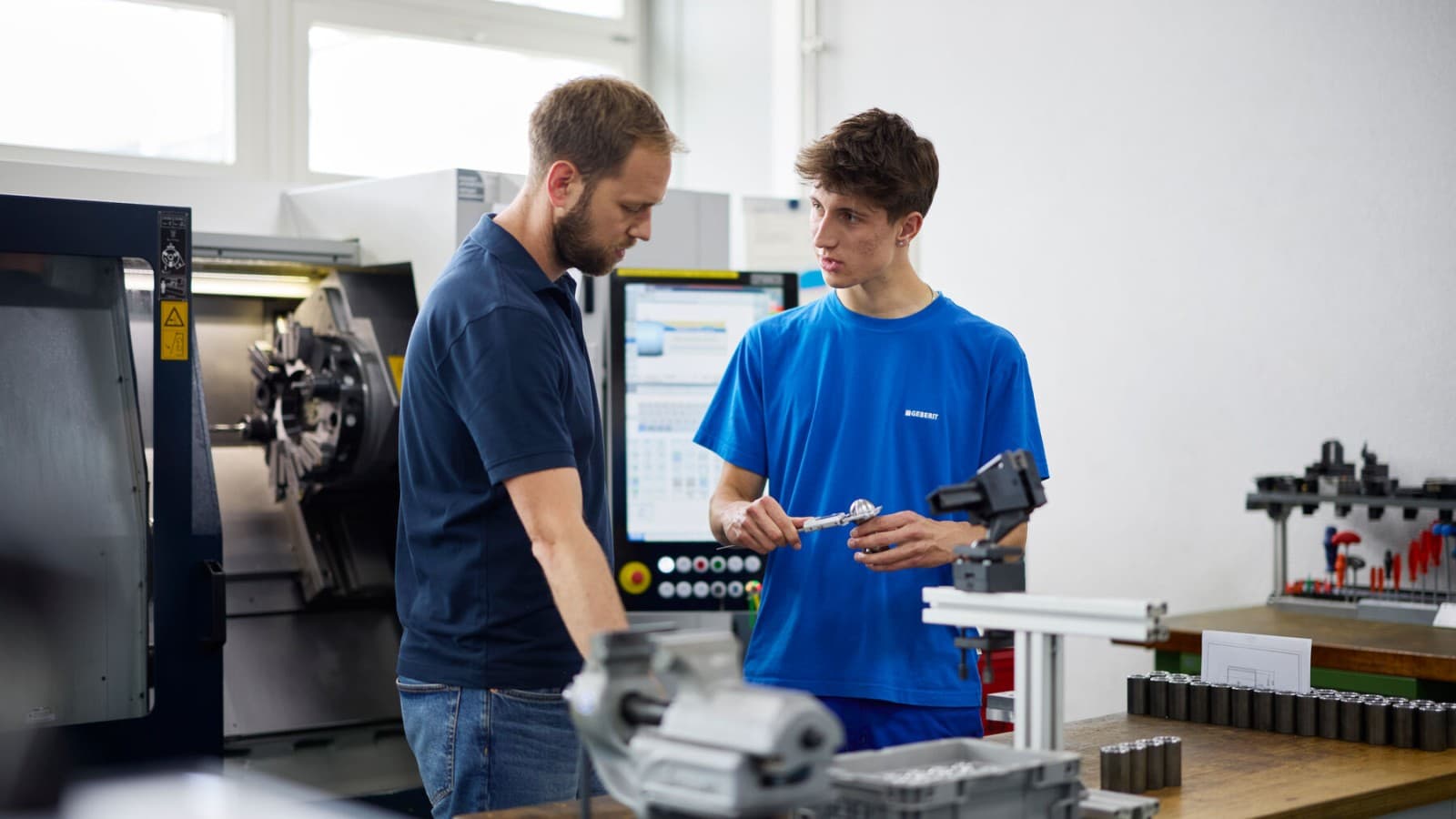 Ein Lernender bei Geberit erhält in der Werkstatt eine Einführung durch seinen Ausbildner Ein Lernender bei Geberit erhält in der Werkstatt eine Einführung durch seinen Ausbildner