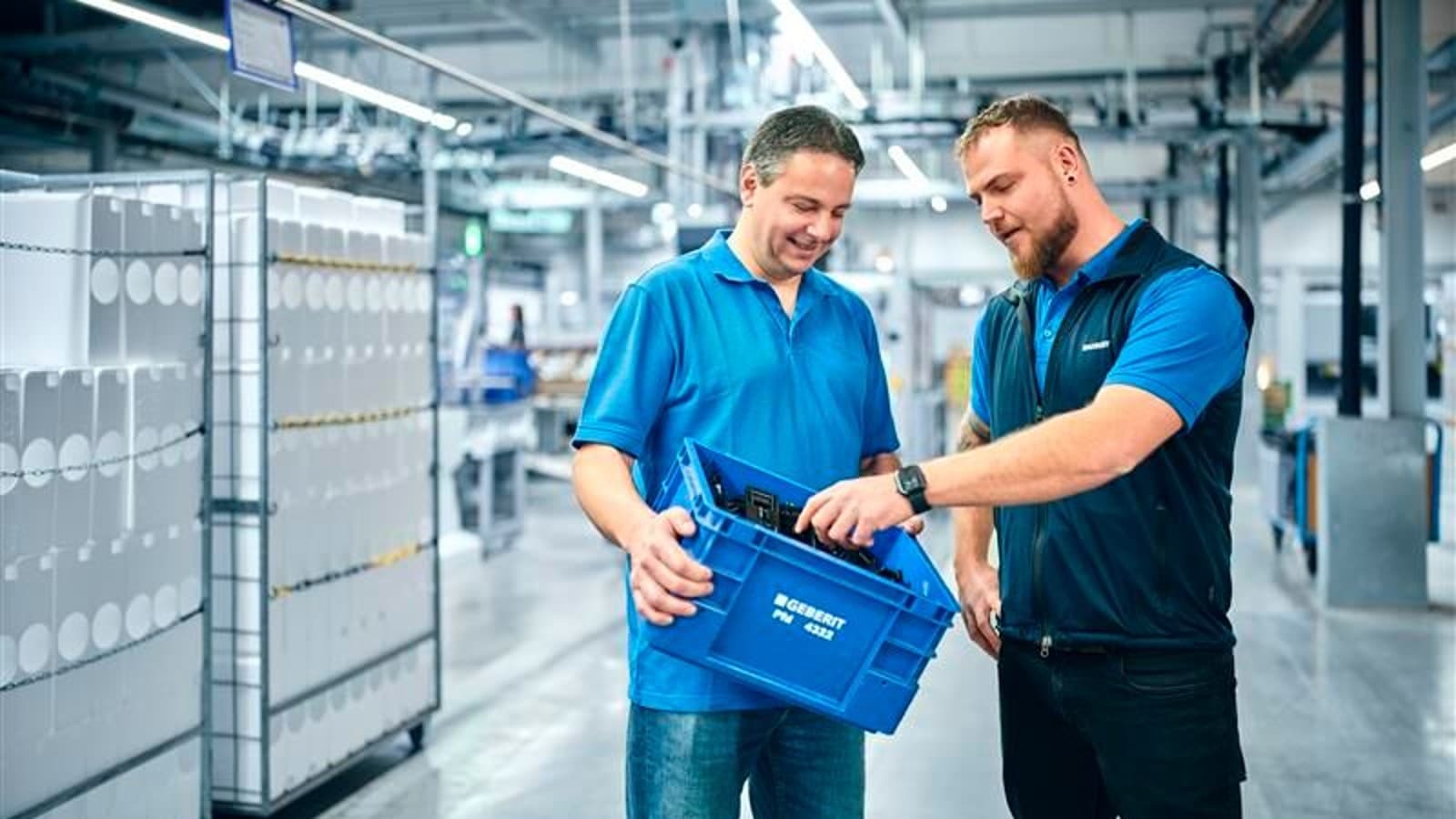 Deux employés inspectent des produits Geberit dans une caisse bleue Deux employés inspectent des produits Geberit dans une caisse bleue