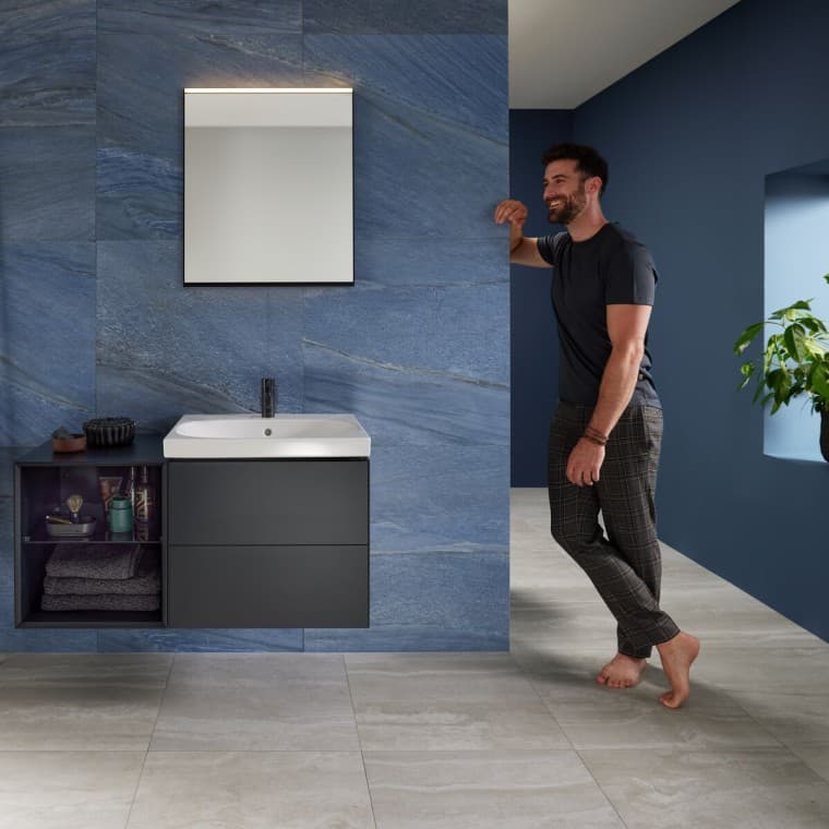 Homme appuyé contre le mur dans une salle de bains bleue avec espace lavabo Geberit Mix & Match Homme appuyé contre le mur dans une salle de bains bleue avec espace lavabo Geberit Mix & Match