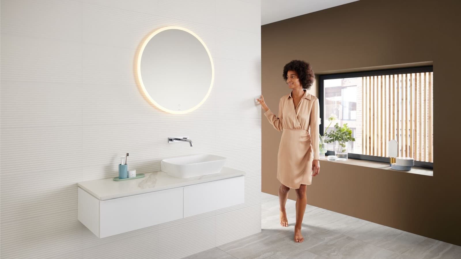 Donna in un bagno dalle tonalità di marrone di tendenza, con una combinazione di zona lavabo Mix & Match Donna in un bagno dalle tonalità di marrone di tendenza, con una combinazione di zona lavabo Mix & Match